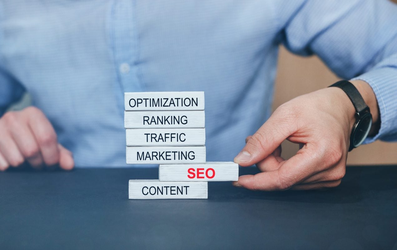 Hand stacking wooden blocks labelled Optimization, Ranking, Traffic, Marketing, SEO and Content